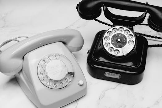 Black and white image of two vintage rotary dial telephones on a marble surface.